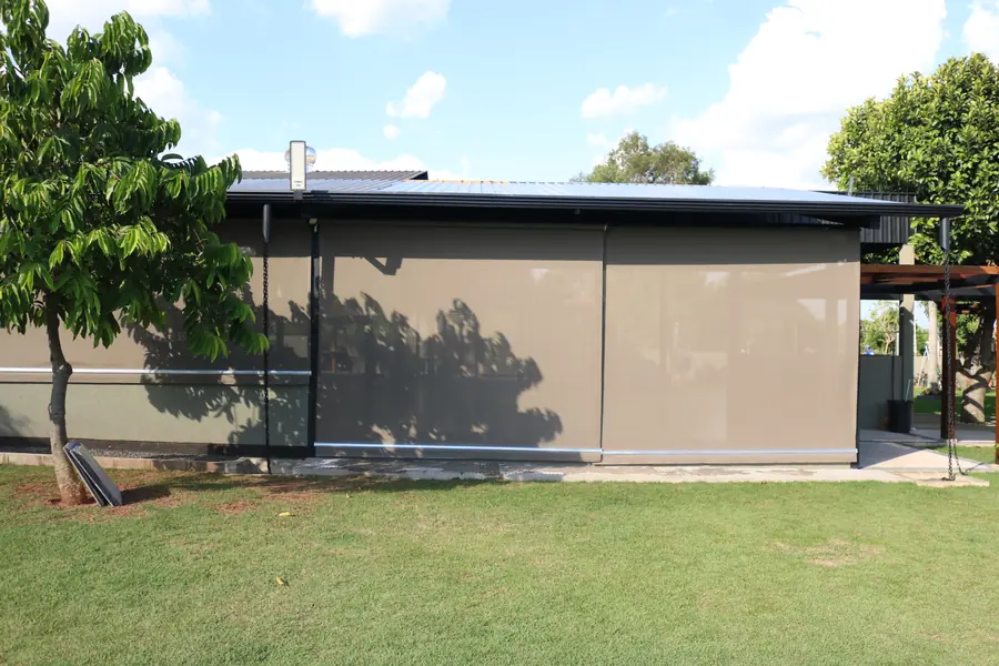 Área externa fechada com cortinas verticais bege, vista do jardim